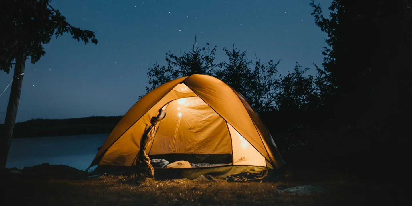 A warmly lit tent under a starry sky with no campfire burning