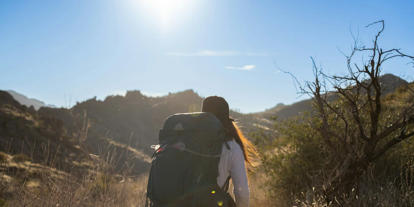 A backpacker with a loaded pack moving through warm early-morning light