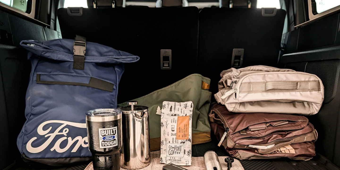 An organized car trunk with folded bedding, a compact kitchen bin, and camp supplies arranged by use