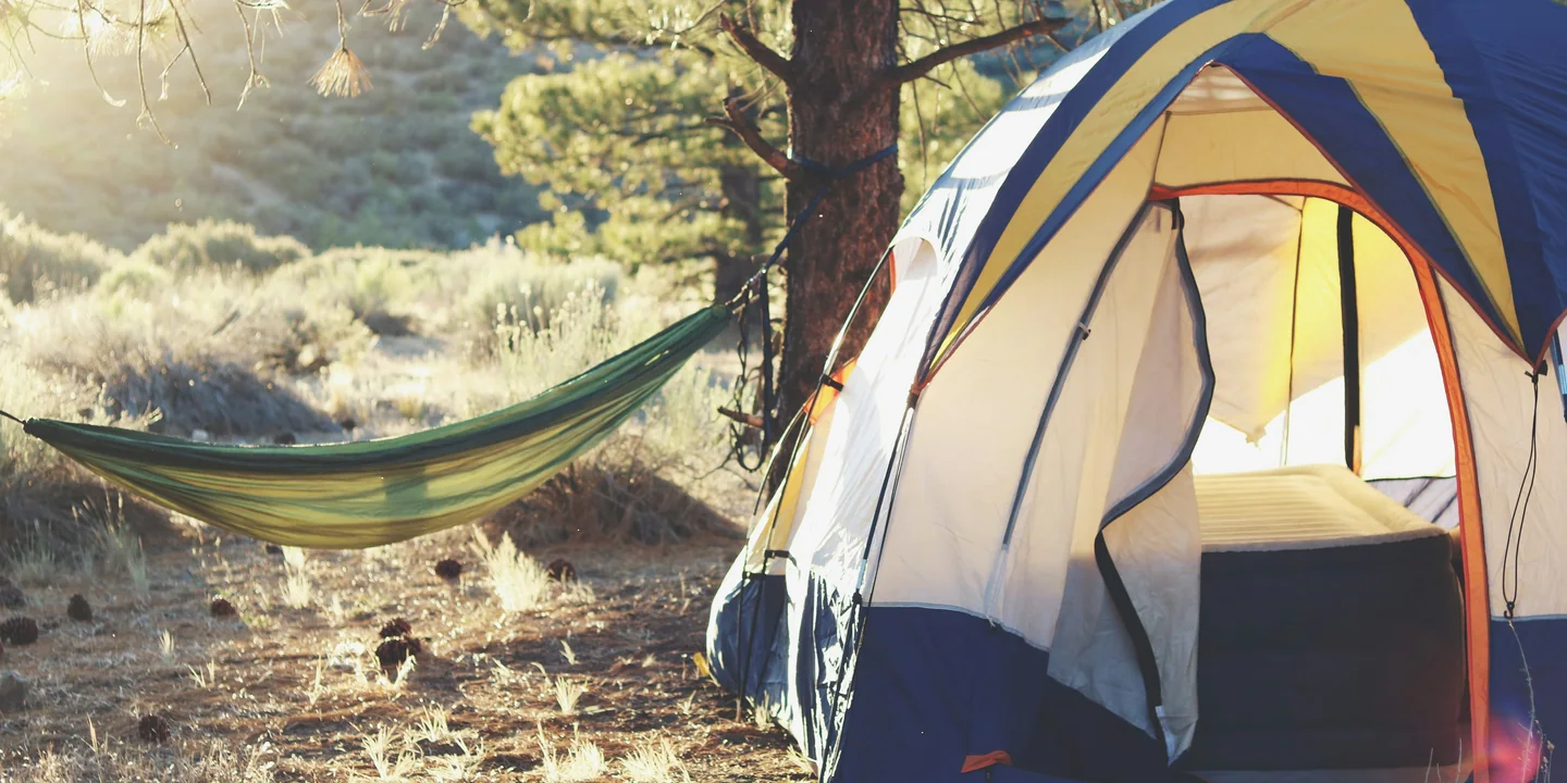 A ventilated tent with its door open beside a hammock in warm evening light