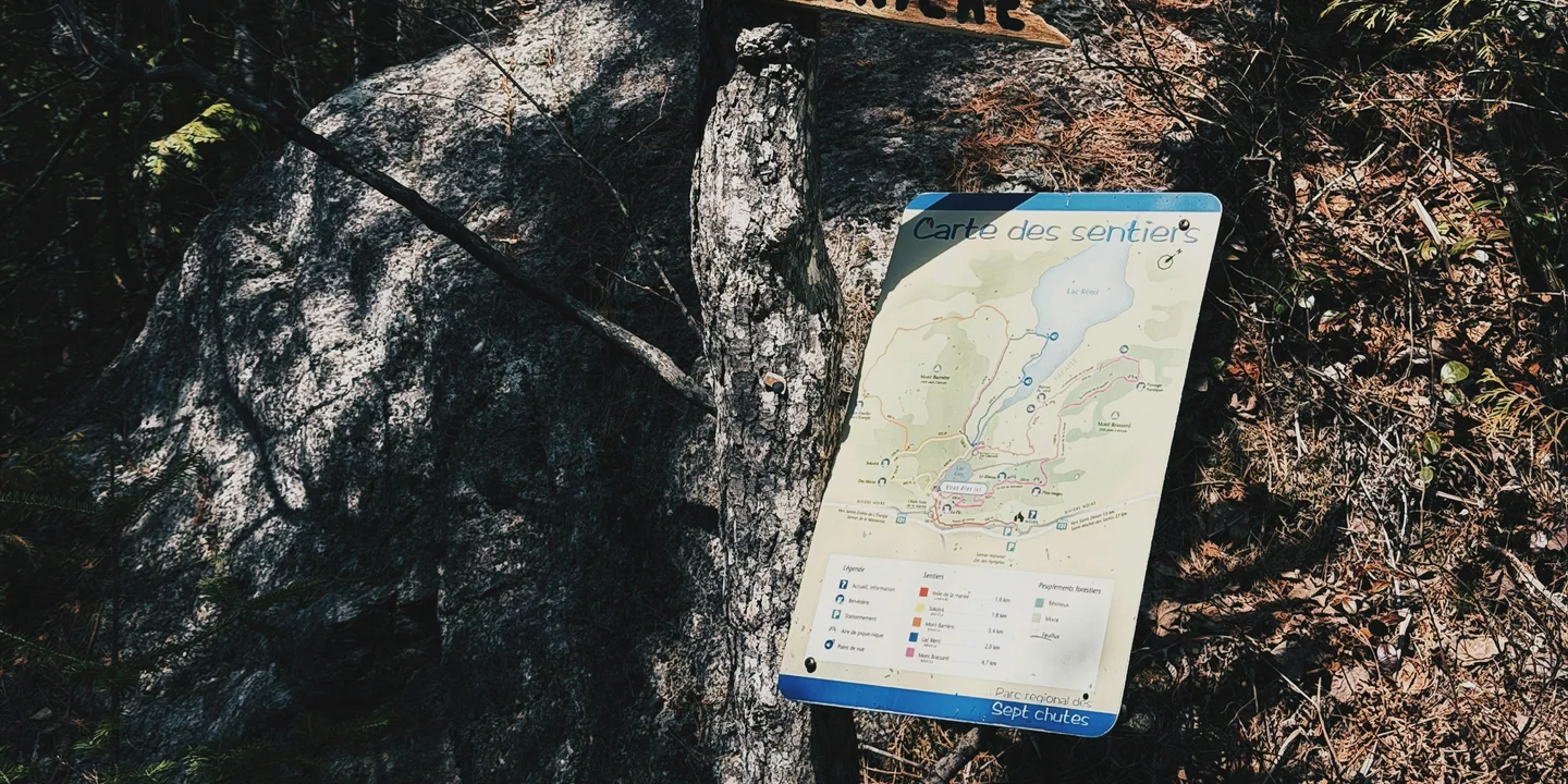 A trail map posted beneath a wooden junction sign in a forest