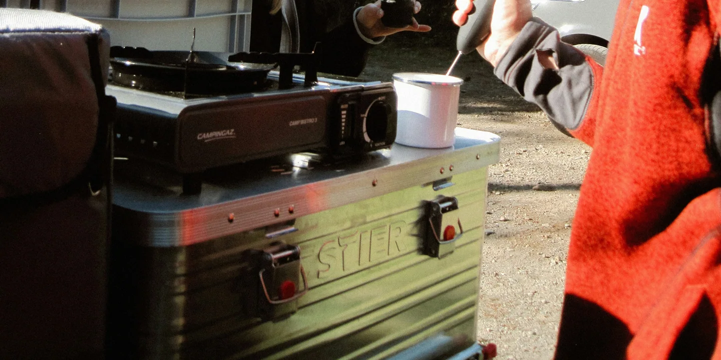 A compact camp stove, kettle, mug, and small cooking kit arranged at a campsite